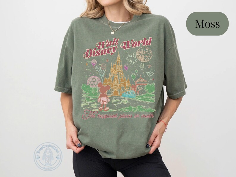Puede incluir: Camiseta verde musgo con un dise&ntilde;o vintage de Walt Disney World. El dise&ntilde;o incluye un castillo, Mickey Mouse y el texto "The Happiest Place on Earth". La camiseta tiene un corte holgado.