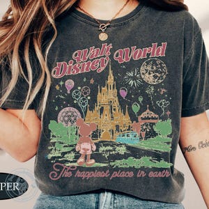 Puede incluir: Camiseta gris oscuro con un gr&aacute;fico colorido del castillo de Walt Disney World, Mickey Mouse y fuegos artificiales. El texto "Walt Disney World" y "The happiest place in earth" se muestra en un estilo vintage.
