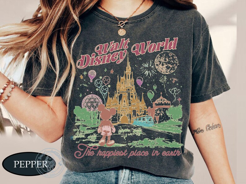 Puede incluir: Camiseta gris oscuro con un gr&aacute;fico colorido del castillo de Walt Disney World, Mickey Mouse y fuegos artificiales. El texto "Walt Disney World" y "The happiest place in earth" se muestra en un estilo vintage.