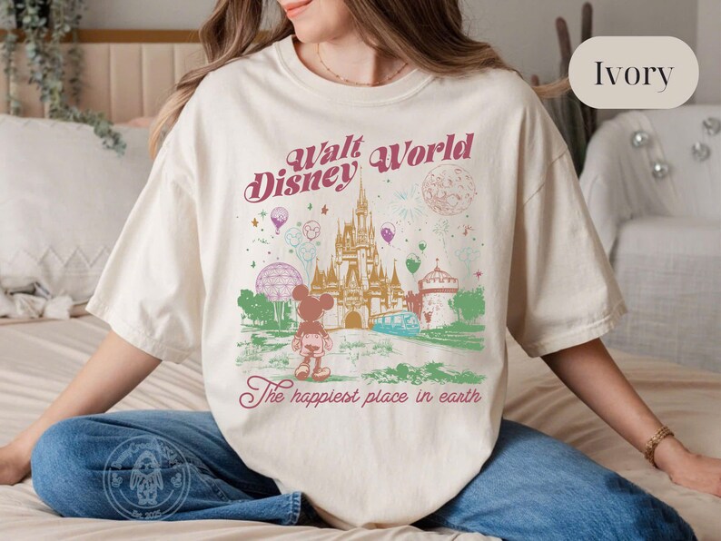 Puede incluir: Camiseta de color marfil con un gr&aacute;fico colorido de Walt Disney World. El dise&ntilde;o incluye un castillo, Mickey Mouse y el texto "Walt Disney World" y "The happiest place in earth."