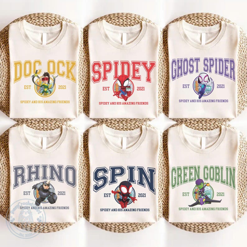 May include: Six cream-colored t-shirts with different superhero-themed designs. Each shirt features a character name in a collegiate font, the year "2021", and the phrase "Spidey and His Amazing Friends".
