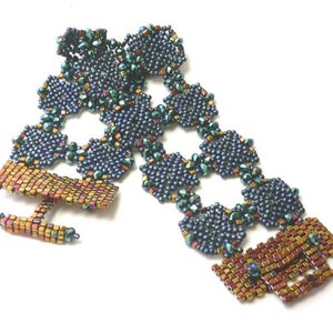 May include: A beaded bracelet with a geometric design featuring blue, green, and gold beads. The bracelet has a clasp closure.