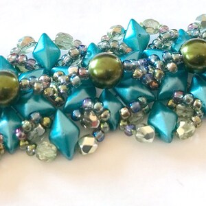 Peut inclure: Un bracelet en perles turquoise et vertes avec un motif en étoile. Le bracelet est fait de petites perles facettées et de perles rondes plus grandes.