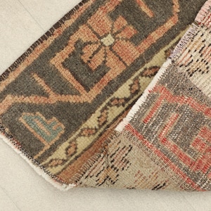 May include: Close-up of a section of a vintage rug with a geometric pattern. The rug features a combination of colors, including brown, orange, beige, and touches of teal. The design includes stylized floral and geometric shapes.