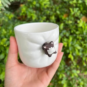 May include: White ceramic mug with a textured surface and a small brown ceramic animal figurine attached to the side.