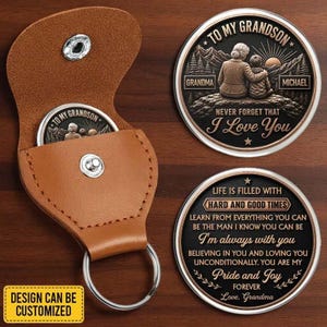 Peut inclure: Un étui porte-clés en cuir beige avec un bouton-pression argenté, contenant une pièce métallique ronde. Deux autres pièces métalliques rondes sont présentées, l'une illustrant une grand-mère et son petit-fils avec le texte TO MY GRANDSON NEVER FORGET THAT I LOVE YOU, et l'autre avec le texte LIFE IS FILLED WITH HARD AND GOOD TIMES.