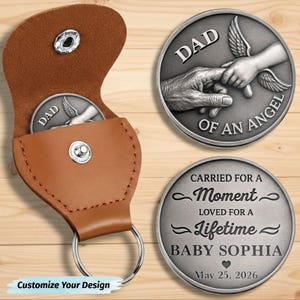 May include: A tan leather pouch with a silver snap button and keyring, containing a round silver coin. The coin features an embossed image of a hand holding a small hand with wings and the text DAD OF AN ANGEL and CARRIED FOR A MOMENT LOVED FOR A LIFETIME BABY SOPHIA May 25, 2026.