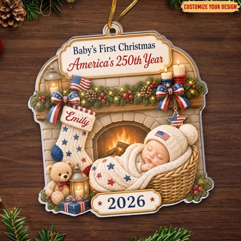 May include: A decorative ornament featuring a fireplace scene with a baby in a basket, a stocking labeled Emily, a teddy bear, and a lantern. The text reads Baby's First Christmas, America's 250th Year, and 2026. It includes red, white, and blue accents.