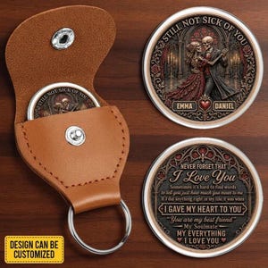 May include: A tan leather keychain pouch with a silver snap button and a circular metal insert featuring a skeleton couple dancing, the names Emma and Daniel, and the text Still Not Sick Of You. A second circular metal insert displays romantic text.