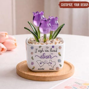 May include: A white square ceramic planter containing three purple glass tulip flowers set in small white stones. The planter features the text "I wish we lived closer" with outlines of South Carolina and Texas, and the names "Jennifer" and "Anna".