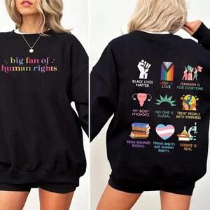 May include: Black sweatshirt with the text "big fan of: human rights" in rainbow colors on the front. The back features various graphics and phrases, including "Black Lives Matter," "Love is Love," and "Feminism is for Everyone."