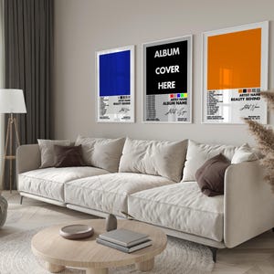 May include: Three rectangular wall posters in white frames displayed in a row. The posters feature minimalist graphic designs with solid color blocks in blue, black, and orange, accompanied by tracklist text and artist name placeholders.