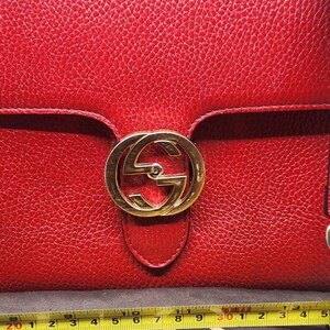 May include: A red leather purse with a gold interlocking GG logo on the front flap. The purse is made of textured leather and has a gold-toned clasp.