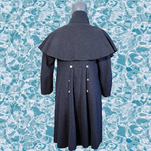 Könnte beinhalten: Ein langer, dunkelgrauer Mantel mit einem großen Kragen und einer Kapuze. Der Mantel hat einen taillierten Oberkörper und einen fließenden Rock. Der Mantel wird mit Knöpfen vorne geschlossen.