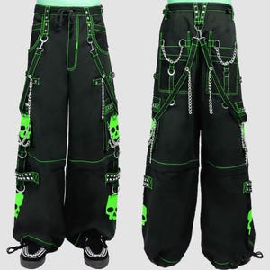 May include: Black cargo pants with neon green stitching and skull graphics. The pants feature multiple pockets, chains, and straps. The design includes a drawstring waist and decorative metal accents.