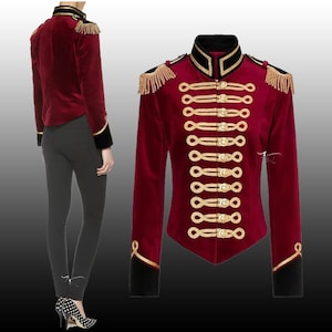 Puede incluir: Una chaqueta de terciopelo rojo con ribetes y botones dorados. La chaqueta tiene un cuello alto y mangas largas. Las mangas tienen un ribete negro en los puños. La chaqueta tiene una silueta ajustada.
