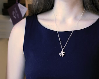 May include: A silver necklace with a unique, abstract pendant. The pendant has a cluster design. The necklace is worn over a dark blue sleeveless top. The chain is delicate and the pendant is small.