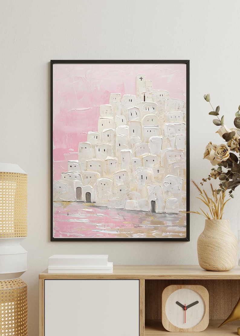 May include: A painting of a white city with a pink sky. The city is made up of many small, white buildings with windows and doors. The sky is a soft pink color with a few clouds. The painting is framed in black.