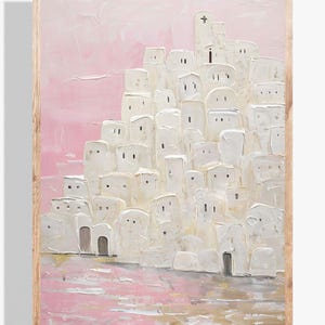May include: A framed painting of a white village with a pink sky. The village is made up of many small, white buildings with windows and doors. The sky is a soft pink color with a hint of gold.