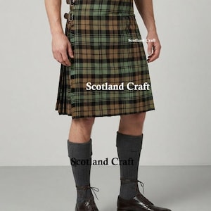 Könnte beinhalten: Ein Kilt mit einem grünen, braunen und schwarzen Schottenkaro-Muster und zwei seitlichen Schnallen an der Taille. Das Kleidungsstück zeigt an drei Stellen den Text Scotland Craft. Dazu werden dunkelgraue Kniestrümpfe und braune Lederschuhe getragen.