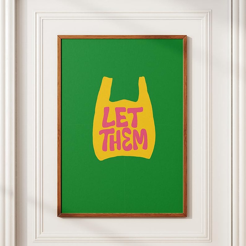 May include: A framed art print with a green backdrop and a yellow shopping bag design. The pink text "LET THEM" is inside the bag. The frame is brown.