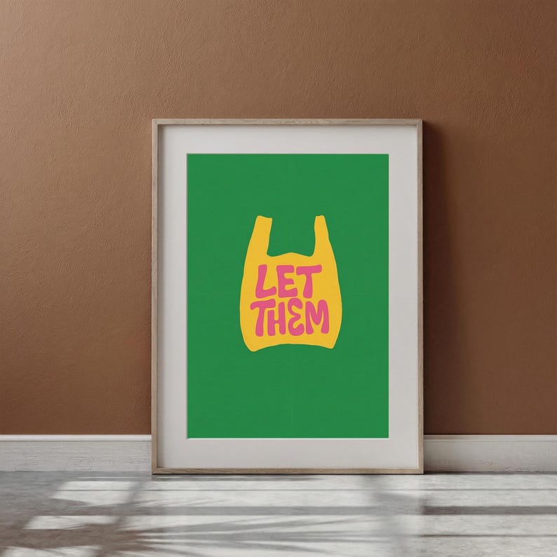 May include: Framed art print with a yellow plastic bag design on a bright green backdrop. The pink text reads "LET THEM". The artwork is displayed on a brown wall, adding a touch of modern decor.