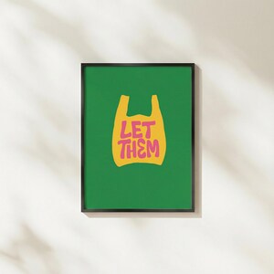 May include: A framed art print with a green background and a yellow shopping bag graphic. The words "LET THEM" are in pink. The print is in a black frame and displayed on a white wall.