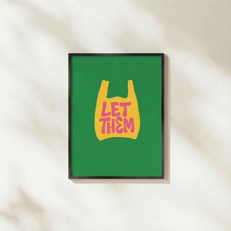 May include: A framed art print with a green background and a yellow shopping bag graphic. The words "LET THEM" are in pink. The print is in a black frame and displayed on a white wall.