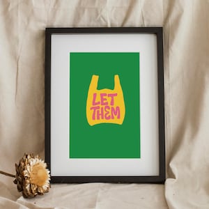 May include: Framed art print with a green background and a yellow shopping bag graphic. The pink text within the bag reads "LET THEM". The black frame surrounds the print. A dried flower is in the lower left corner.