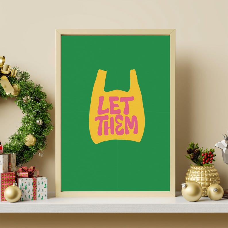 May include: A framed art print with a green background and a yellow shopping bag graphic. The words "LET THEM" are in pink. The print is displayed on a white shelf with Christmas decorations.