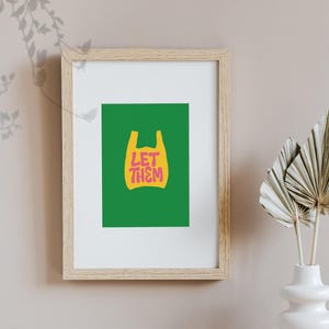 May include: Framed art print with a green backdrop and a yellow plastic bag graphic. The pink text "LET THEM" is inside the bag shape. The frame is made of light-coloured wood.