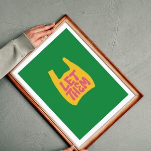 May include: A framed art print with a green background and a yellow plastic bag graphic. The bag has the words "LET THEM" in pink. The frame is brown.