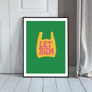 May include: A framed art print with a green background. It features a yellow shopping bag graphic with the pink text "LET THEM". The print is encased in a black frame, suitable for wall display.