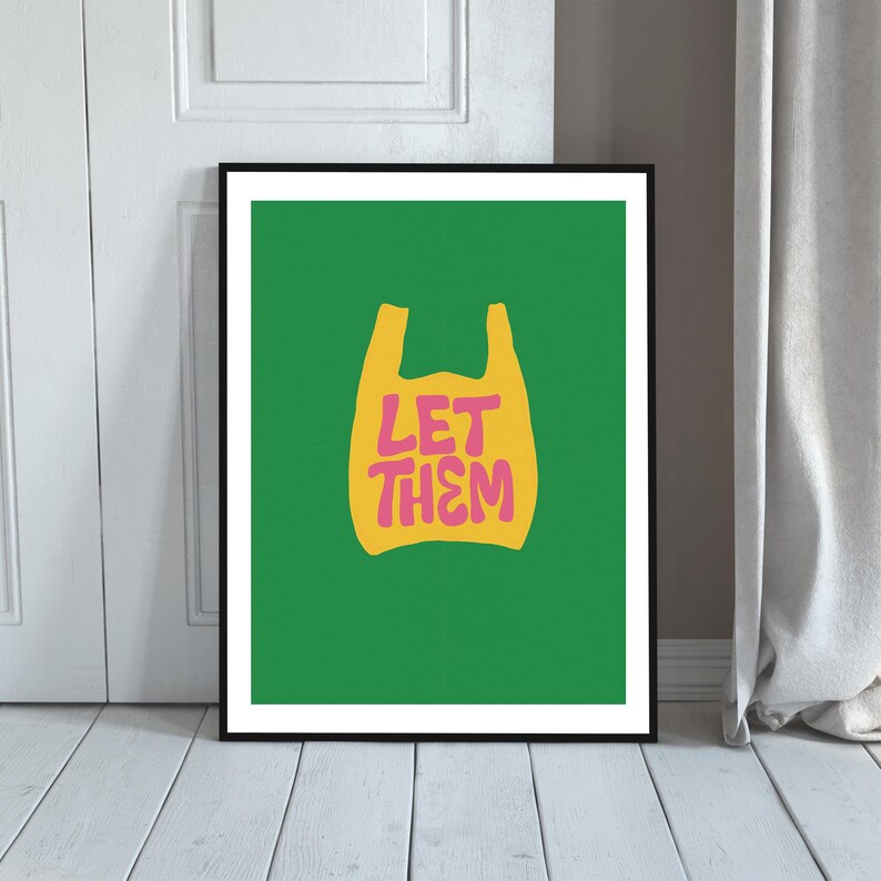 May include: A framed art print with a green background. It features a yellow shopping bag graphic with the pink text "LET THEM". The print is encased in a black frame, suitable for wall display.