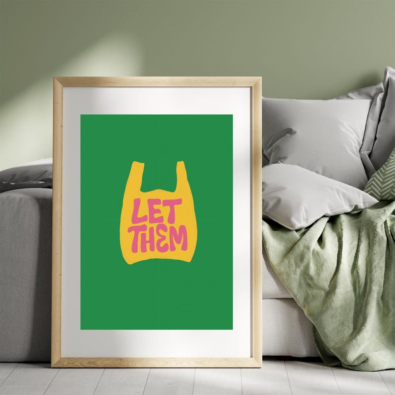 May include: A framed art print with a yellow plastic bag graphic and the pink text "LET THEM". The artwork is set against a vivid green background. The frame is a light wood colour, adding a natural touch to the modern design.