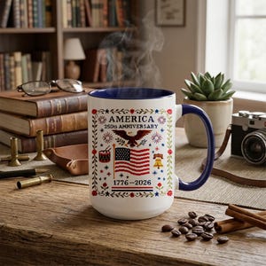 Side angle of the 250th anniversary patriotic mug with handle visible, white ceramic printed with folk-art cross-stitch American flag and eagle for the 2026 semiquincentennial.