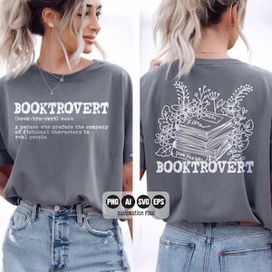 May include: A grey t-shirt with the word "BOOKTROVERT" printed in white. The front of the shirt has a definition of the word. The back of the shirt features a stack of books surrounded by floral elements and the word "BOOKTROVERT".