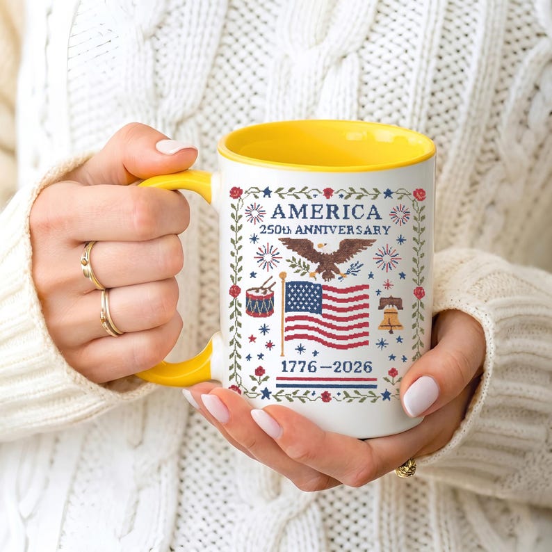 America 250th anniversary mug shown in both 11oz and 15oz sizes, white ceramic with a cross-stitch eagle, flag and Liberty Bell design marking 1776–2026.