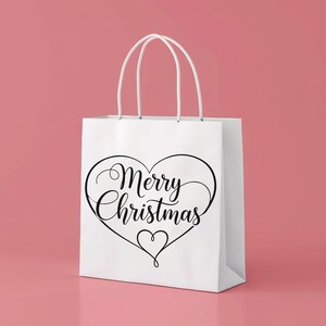 Op de afbeelding: Witte cadeauzak met een zwart hartvormig ontwerp en de woorden "Merry Christmas" in elegant schrift. De tas heeft witte handvatten en staat tegen een roze achtergrond, perfect voor kerstcadeaus.