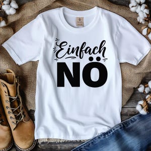 Puede incluir: Camiseta blanca con la frase alemana "Einfach N&Ouml;" impresa en negro. La camiseta tiene cuello redondo y mangas cortas. El texto est&aacute; en negrita, con fuente sans-serif. La camiseta se muestra sobre una superficie texturizada.