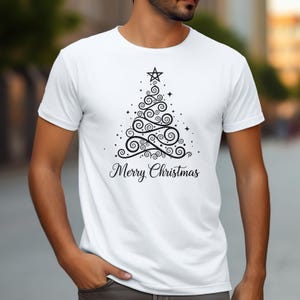 Op de afbeelding: Wit T-shirt met een zwart kerstboomontwerp van krullen, stippen en een ster. De woorden "Merry Christmas" staan eronder in een scriptlettertype. Een feestelijk kledingstuk voor de feestdagen.