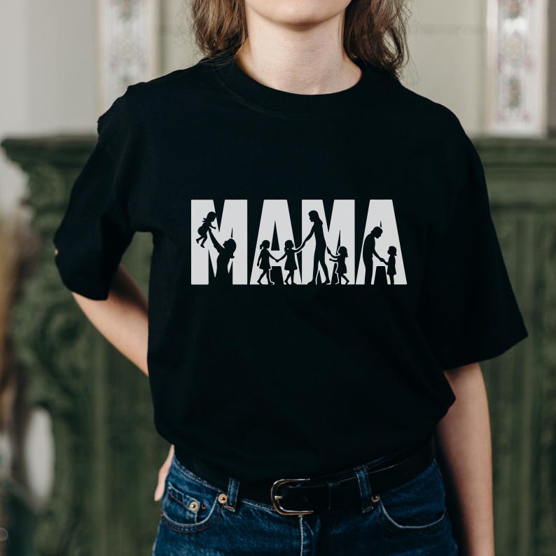 Op de afbeelding: Zwart T-shirt met het woord "MAMA" in witte blokletters. Het woord "MAMA" heeft een silhouetontwerp van een ouder en kinderen. De ouder houdt een kind omhoog en de andere kinderen houden elkaars hand vast.