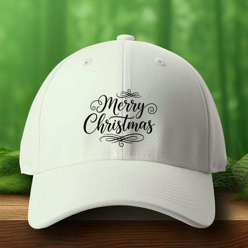 Op de afbeelding: Een witte baseballpet met een gebogen klep. De pet heeft de tekst "Merry Christmas" in een decoratief lettertype. De pet staat tegen een vage groene achtergrond.