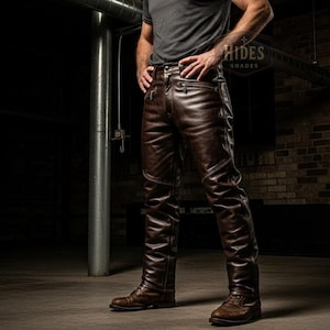 Puede incluir: Pantalones de cuero marr&oacute;n con un corte cl&aacute;sico, con costuras detalladas y una est&eacute;tica robusta. Los pantalones se combinan con botas de cuero marr&oacute;n y una camiseta gris. La imagen est&aacute; ambientada en un espacio industrial con poca luz.