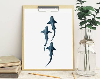 May include: A framed print of a watercolor painting of three blue sharks swimming in a vertical line. The sharks are outlined in black and have a gradient of blue shades.