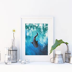May include: A framed print of a black and white whale shark swimming in blue and green water. The print is in a white frame and is sitting on a white shelf with other decorative items.