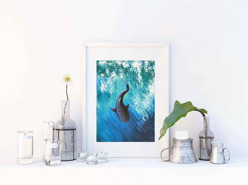 May include: A framed print of a black and white whale shark swimming in blue and green water. The print is in a white frame and is sitting on a white shelf with other decorative items.