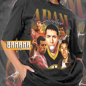 May include: Black unisex t-shirt featuring a collage of Adam Sandler images with the text "Adam Sandler" in gold. The shirt includes the "Banana Gorillas" logo and the phrase "More Colors Available".