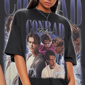 Peut inclure: T-shirt noir unisexe avec un motif "CONRAD" violet et le texte "Fisher". Le t-shirt pr&eacute;sente un collage de quatre hommes. Le t-shirt est surdimensionn&eacute;.