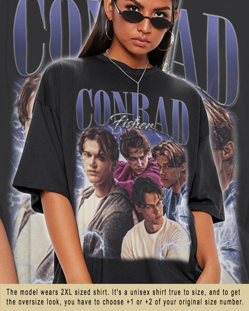 Peut inclure: T-shirt noir unisexe avec un motif "CONRAD" violet et le texte "Fisher". Le t-shirt pr&eacute;sente un collage de quatre hommes. Le t-shirt est surdimensionn&eacute;.